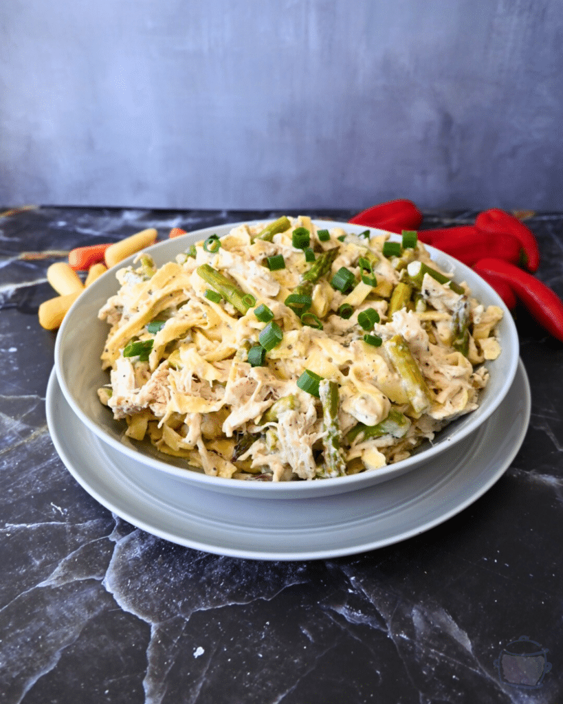 a bowl full of slow cooker caesar chicken pasta with veggies in the background