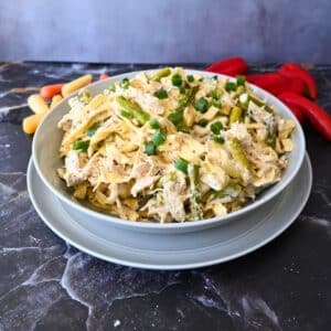 a bowl full of slow cooker caesar chicken pasta with veggies in the background