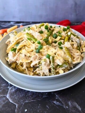 a bowl full of slow cooker caesar chicken pasta with veggies in the background