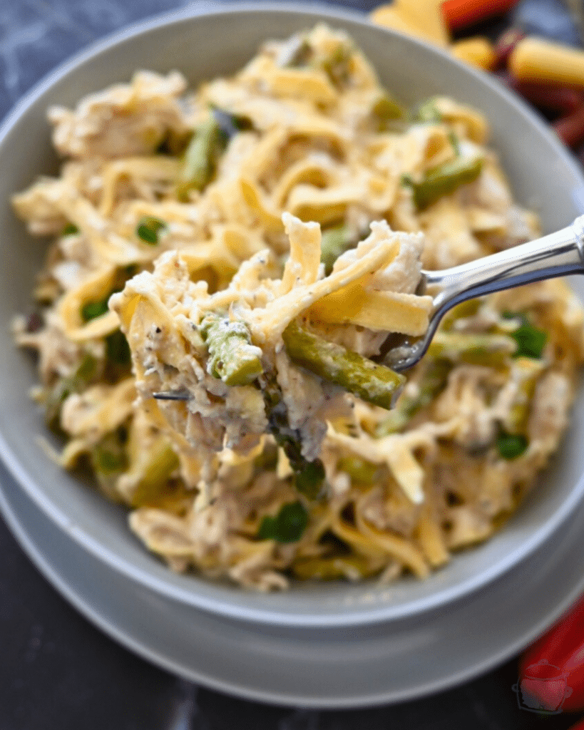 a bowl full of slow cooker caesar chicken pasta some is held up on a fork