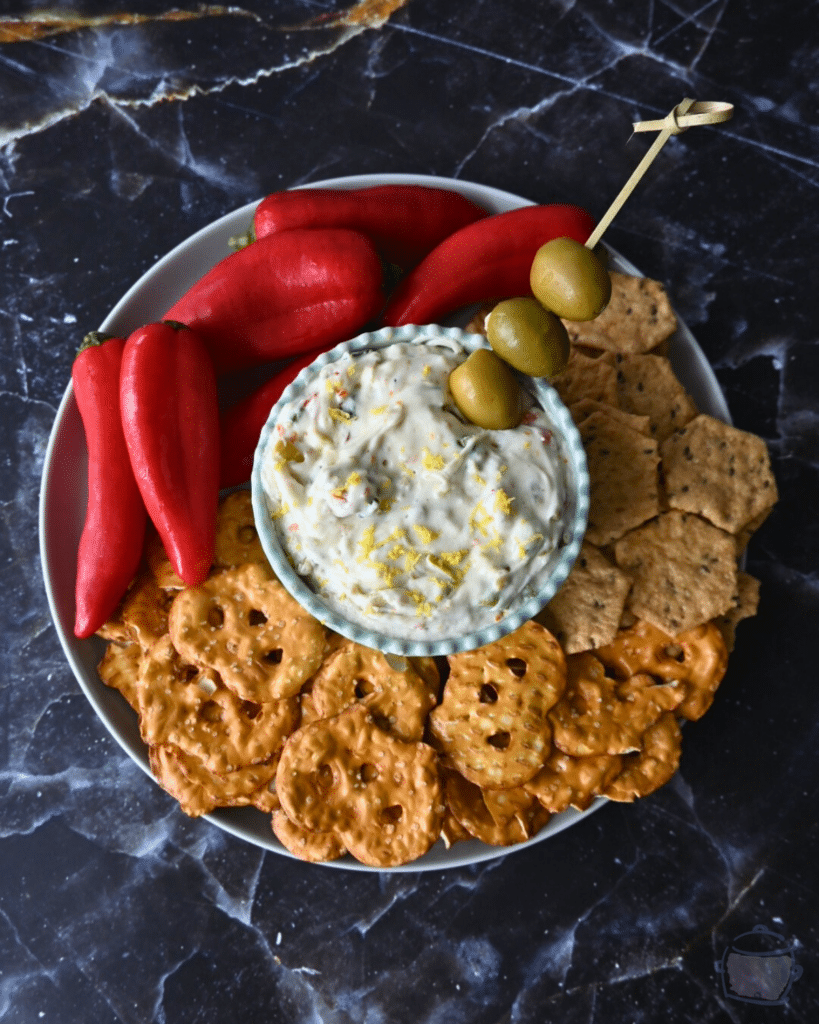 Dirty martini slow cooker dip in a bowl in the middle of pretzels crackers and peppers