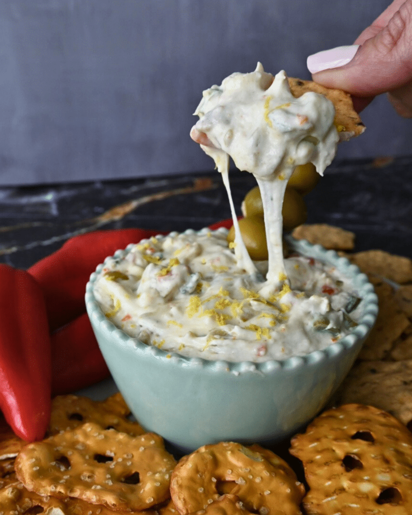 slow cooker dirty martini dip on a cracker over a bowl of the same
