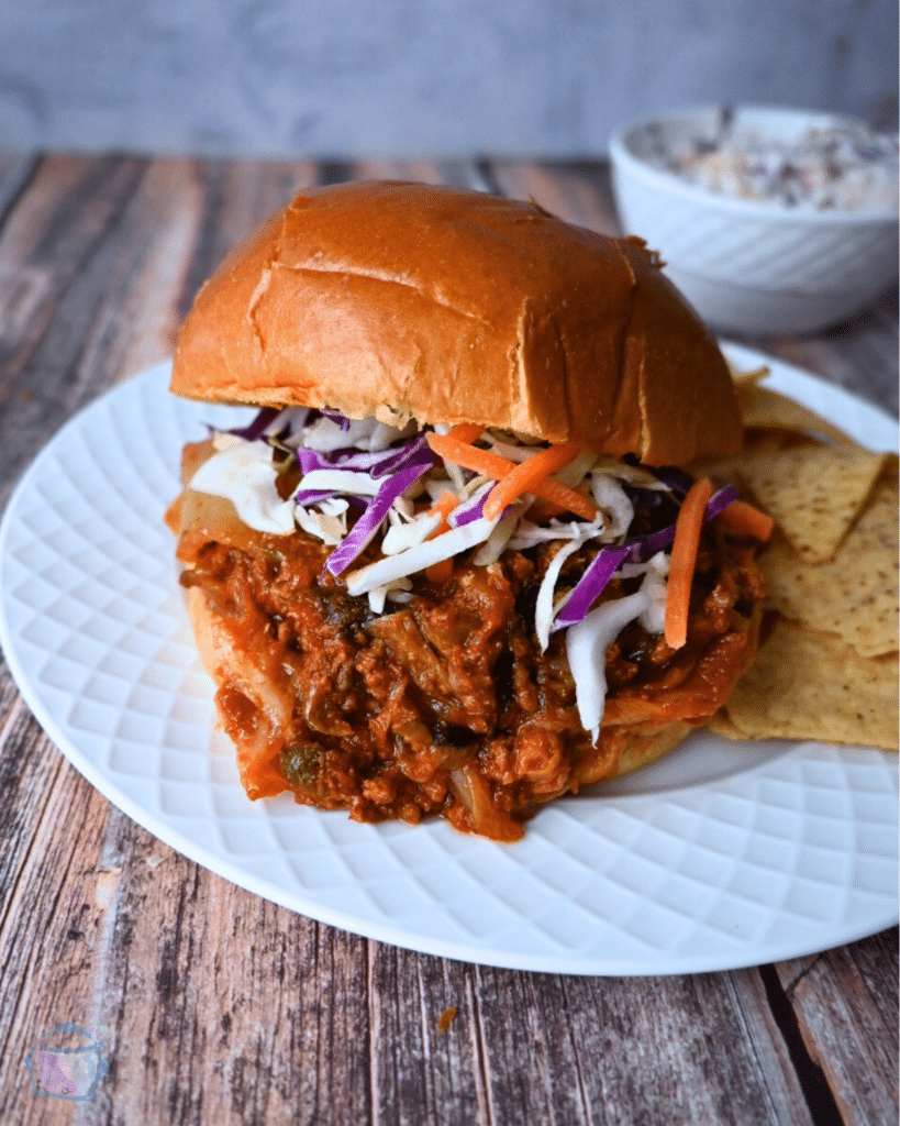 slow cooker kimchi sloppy joe on a brioche roll with a side of chips