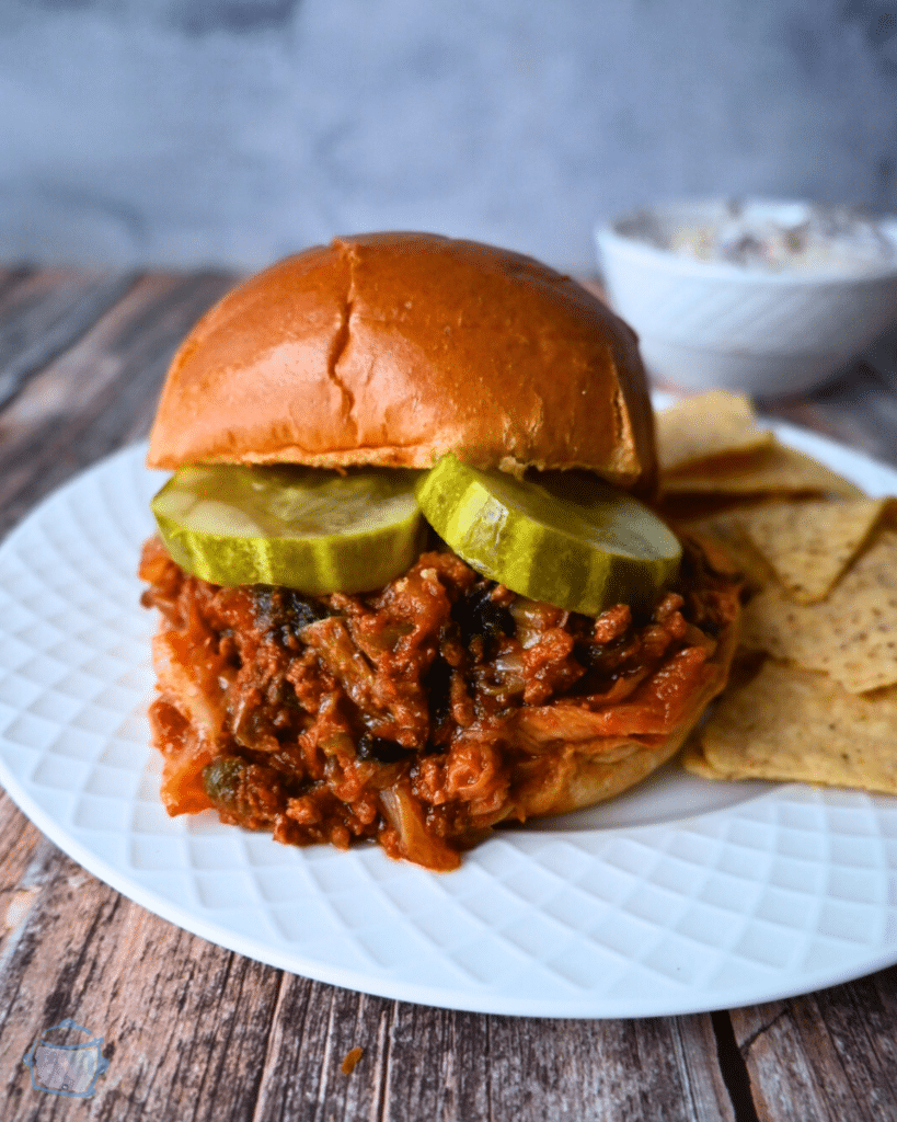 slow cooker kimchi sloppy joe on a brioche roll with a side of chips