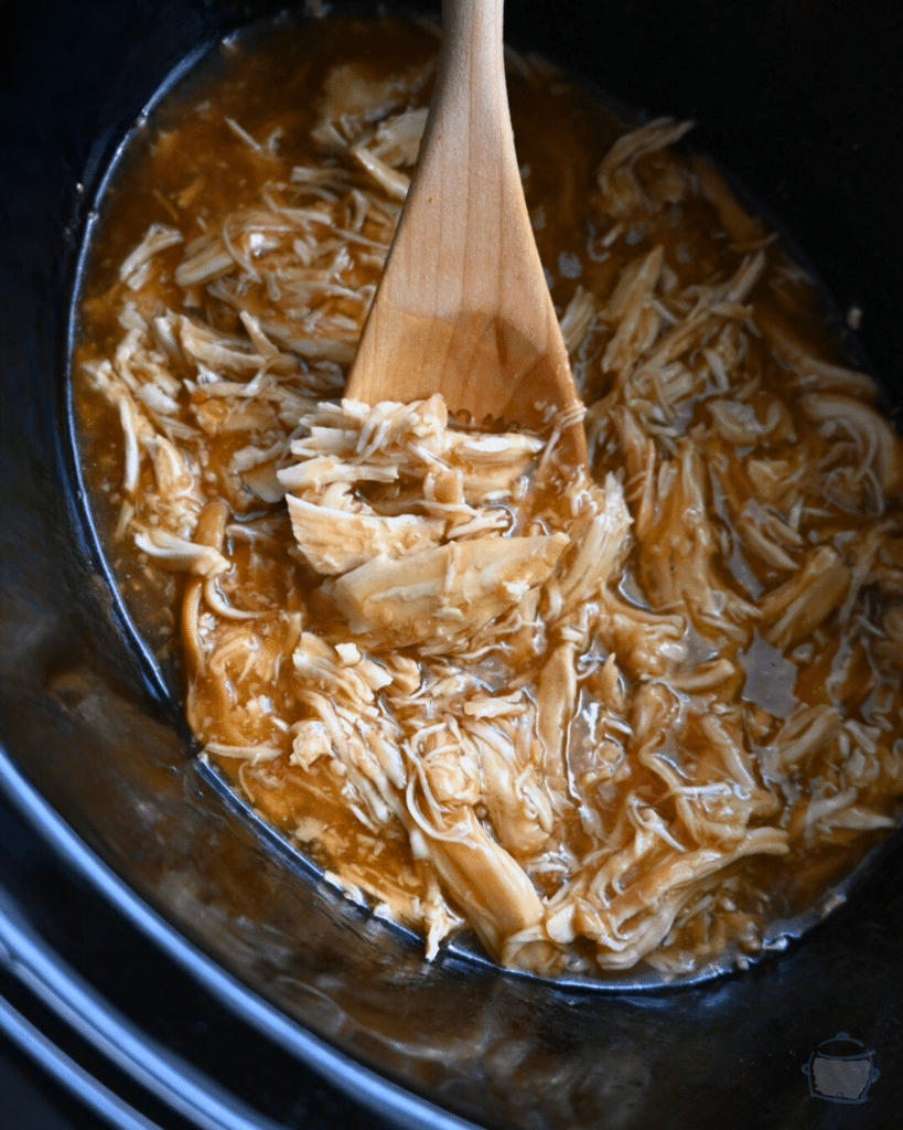 lime maple shredded chicken in crock pot with a wooden spoon
