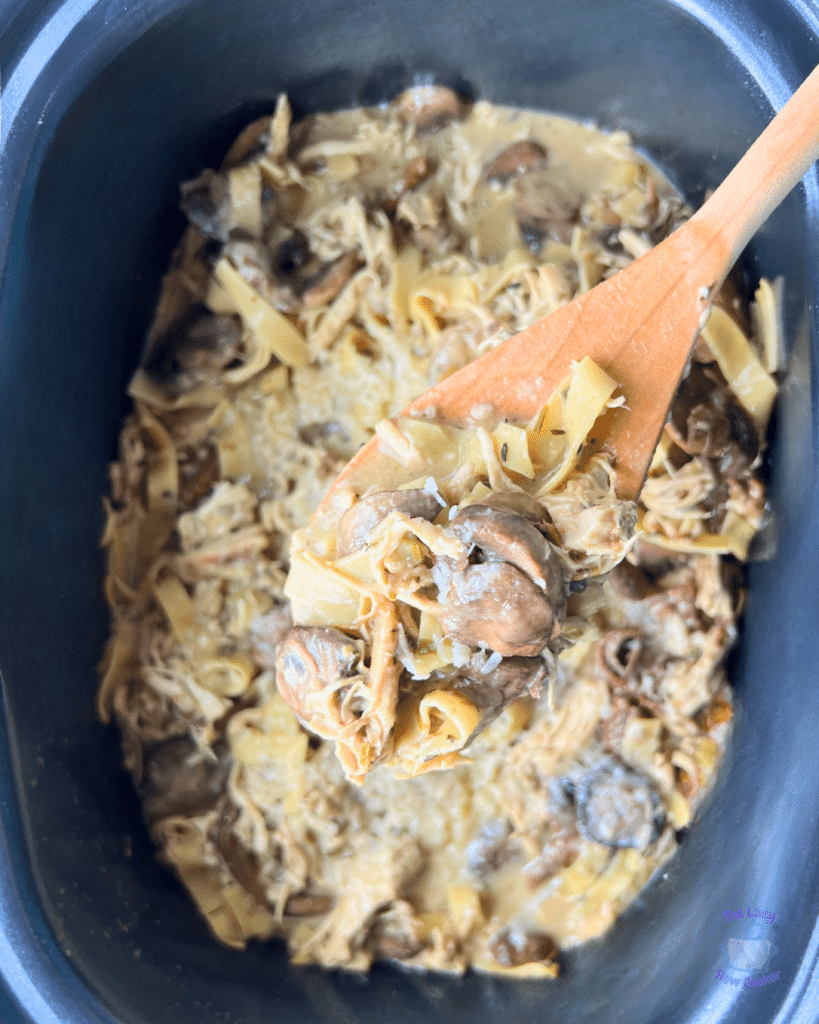 finished creamy mushroom chicken and pasta in a crock pot with some on a wooden spoon in the foreground