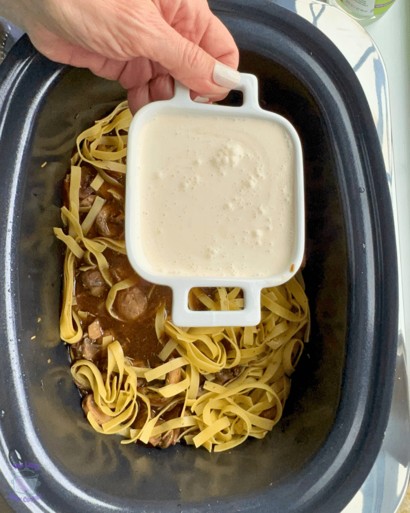 cream in a bowl about to be poured into ingredients in slow cooker