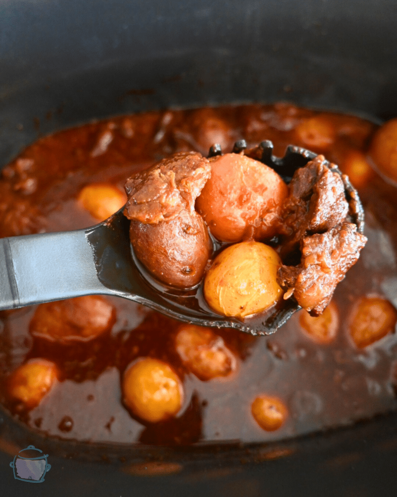 steak bites and potatoes bbq sauce on a spoon held over a slow cooker full of the same