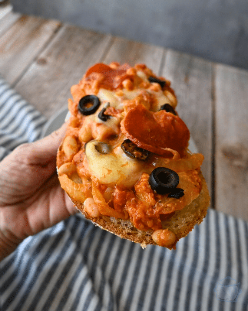 pizza beans on a slice of sour dough bread ready to take a bite.