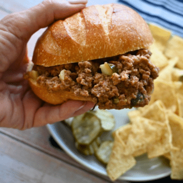 a pickle sloppy joe being held over a plate with chips