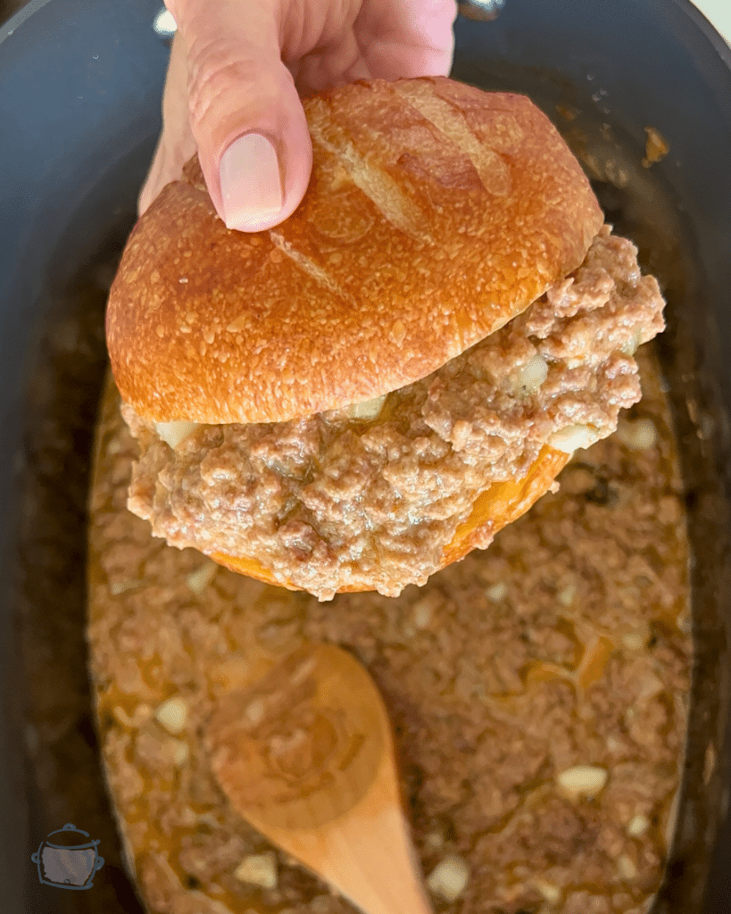a pickle sloppy joe being held over a slow cooker