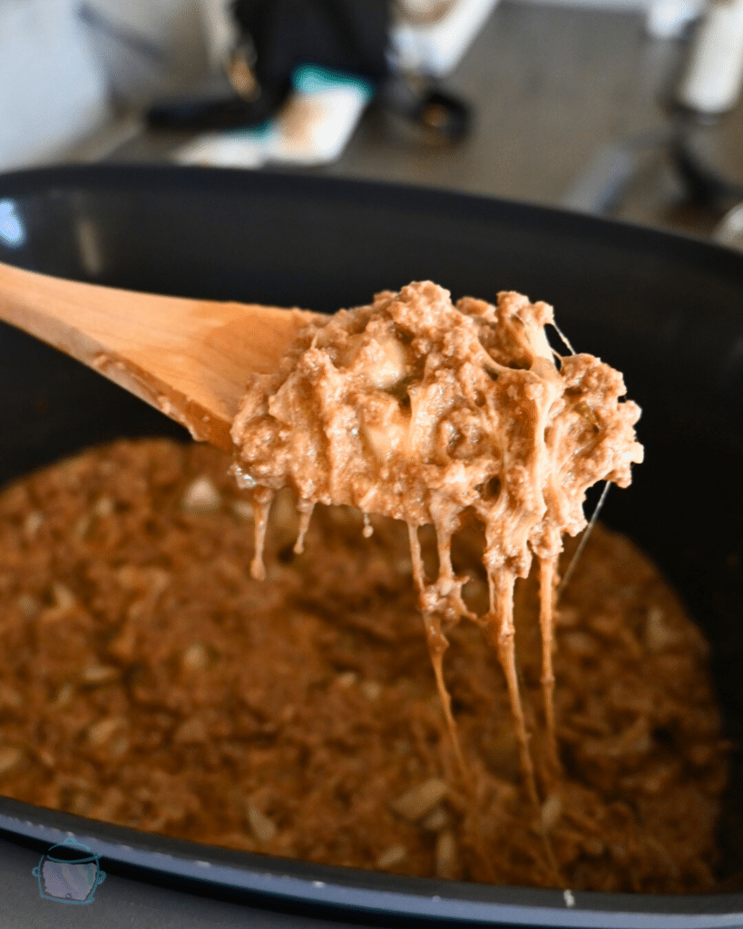 cheesy pickle Joes on a wooden spoon held over a slow cooker of the same