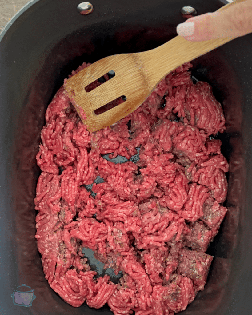 ground beef in a greased crockpot with a wooden spatula
