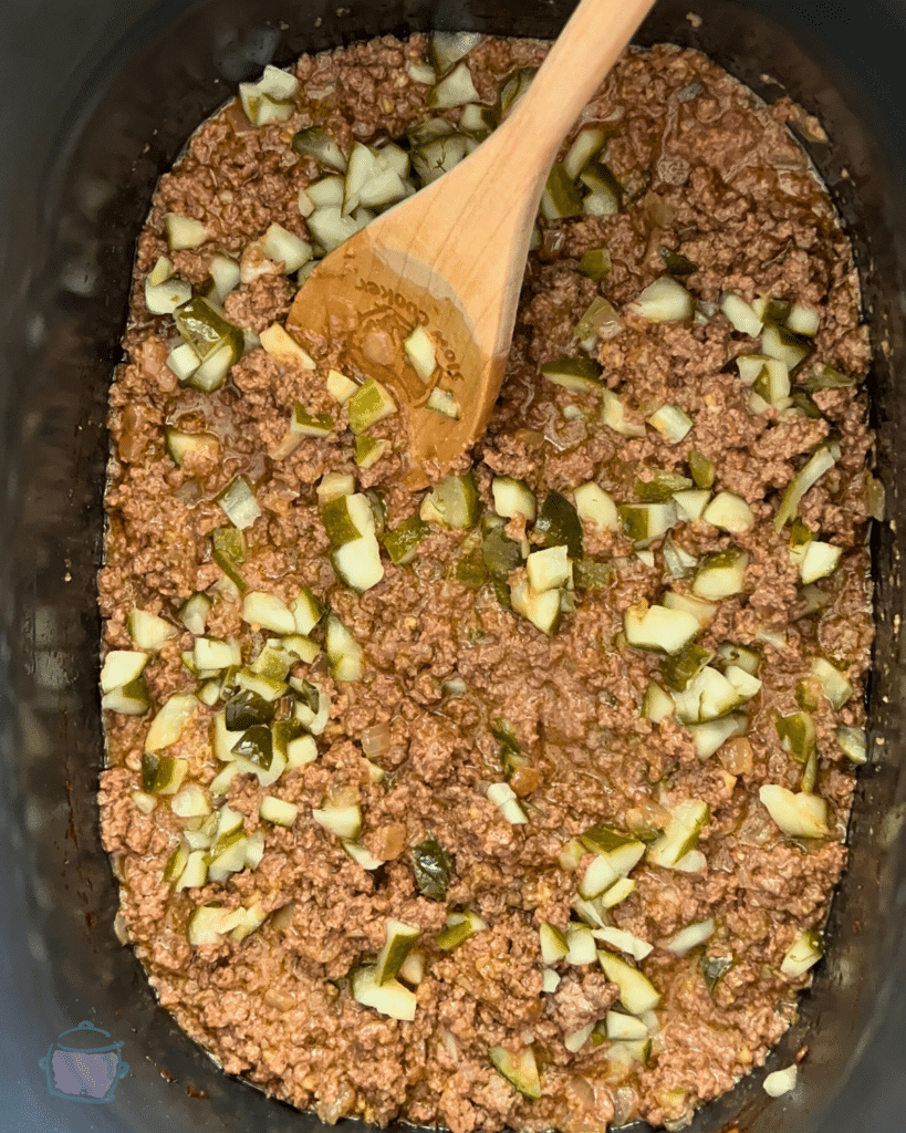 ground beef and seasonings in a slow cooker with dill pickle being added
