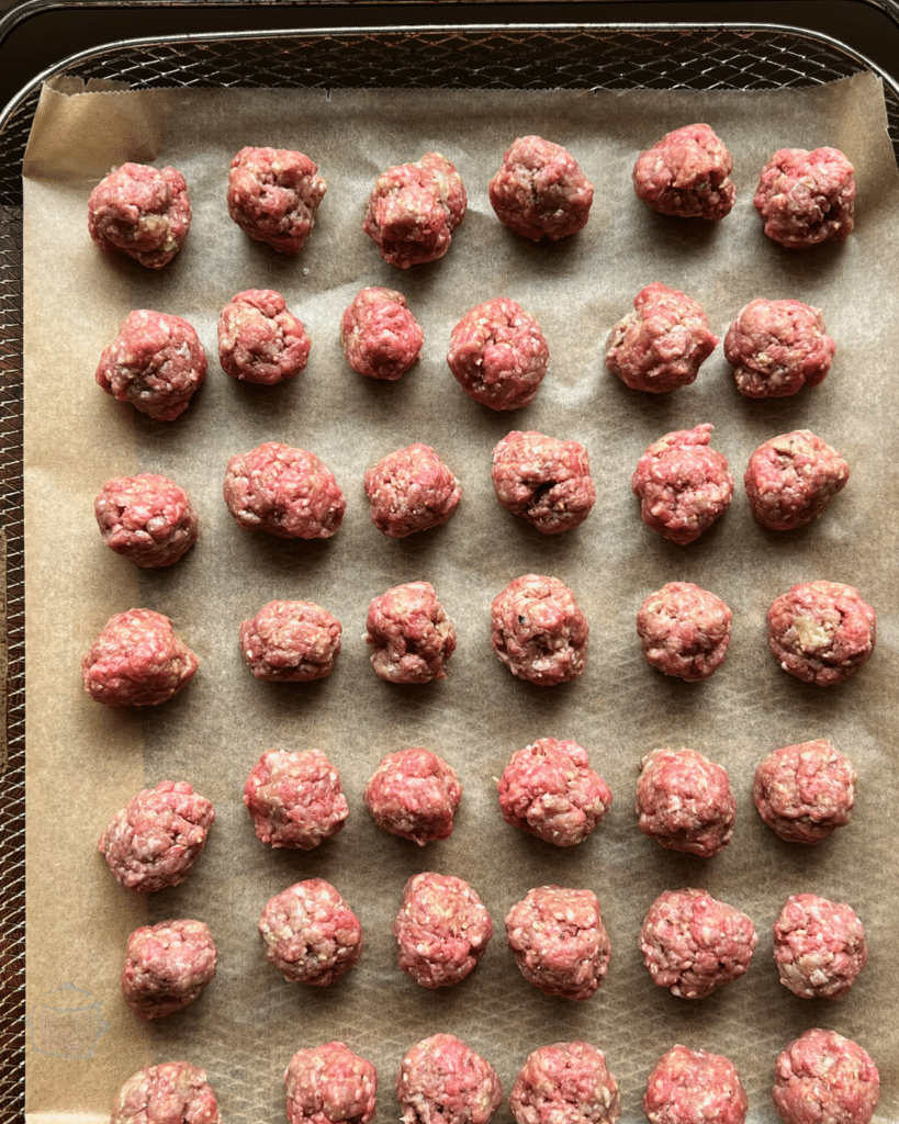 raw meatballs lined up on a an air fryer cooking tray