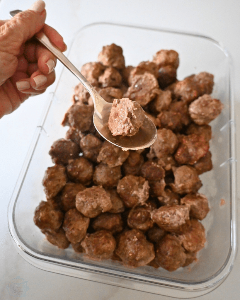cooked meatballs in a freezer safe container with one on a spoon