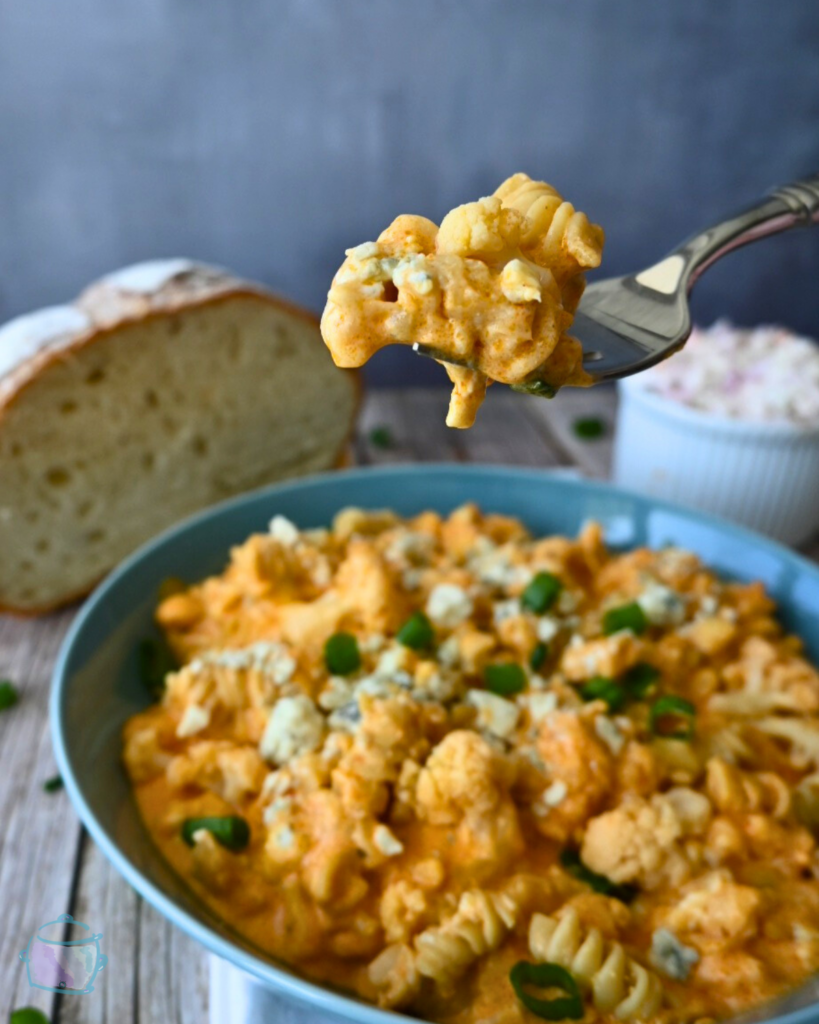 Slow cooker cauliflower buffalo macaroni and cheese on a fork over a bowl full of the same