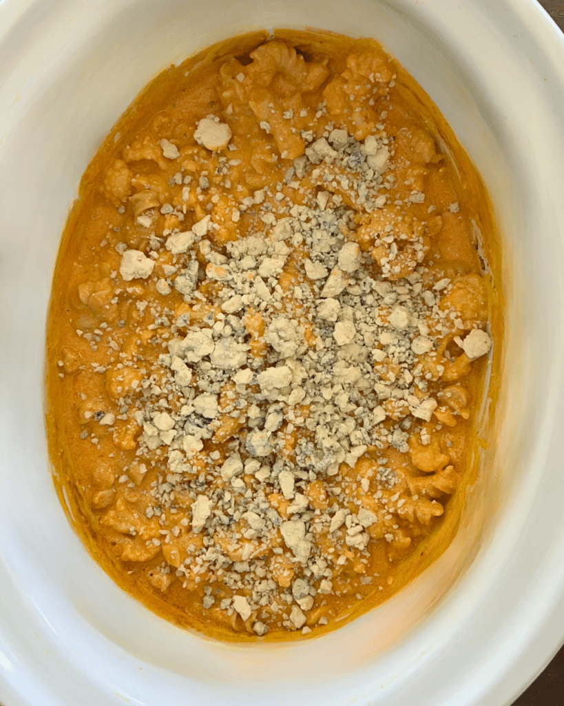 slow cooker full of cauliflower buffalo mac and cheese with blue cheese crumbles