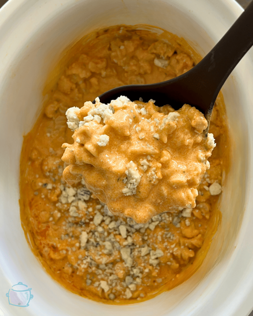 Slow cooker cauliflower buffalo macaroni and cheese on a ladle over a slow cooker full of the same