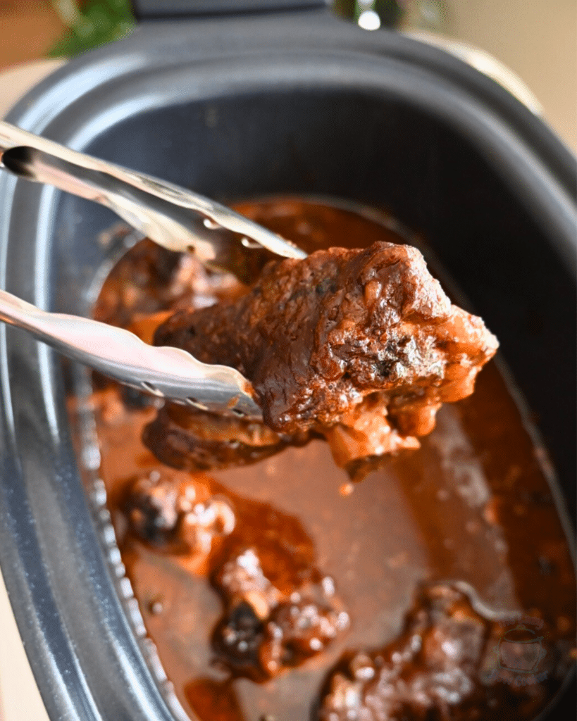 tongs holding a cooked rib over a slow cooker full of the same