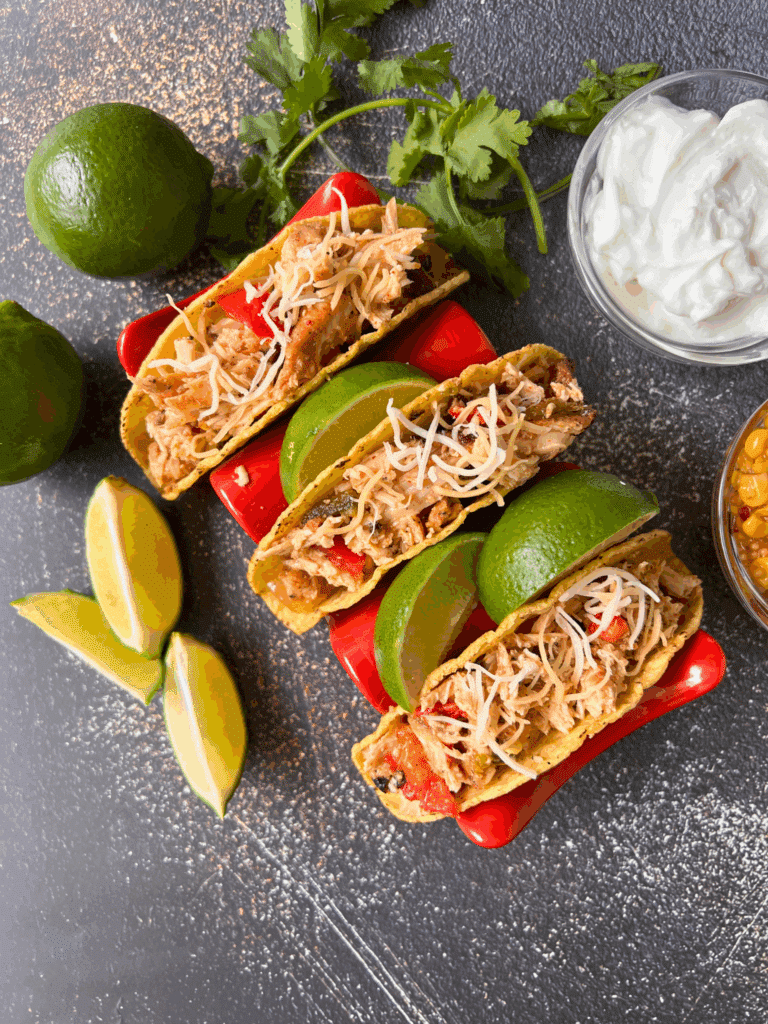 3 crunch slow cooker chicken tacos on a plate with limes wedges and toppings
