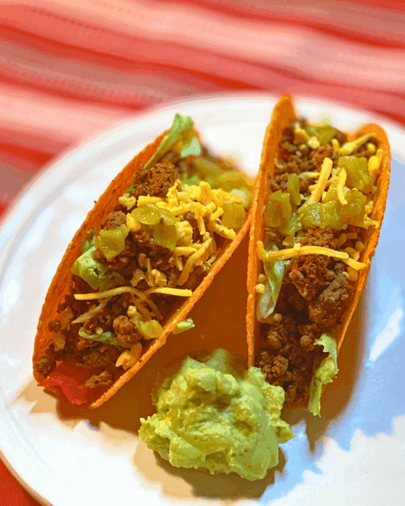 two slow cooker ground beef hard-shell tacos with some guacamole