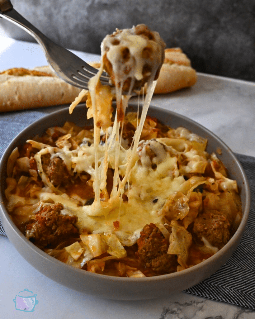 Crockpot cabbage and meatballs topped with melted cheese on a fork over a bowl full of the same