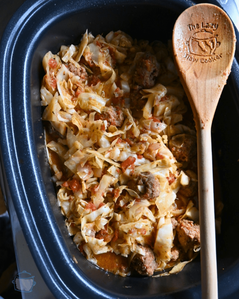 Meatballs and cabbage in a slow cooker with a wooden spoon ready to serve