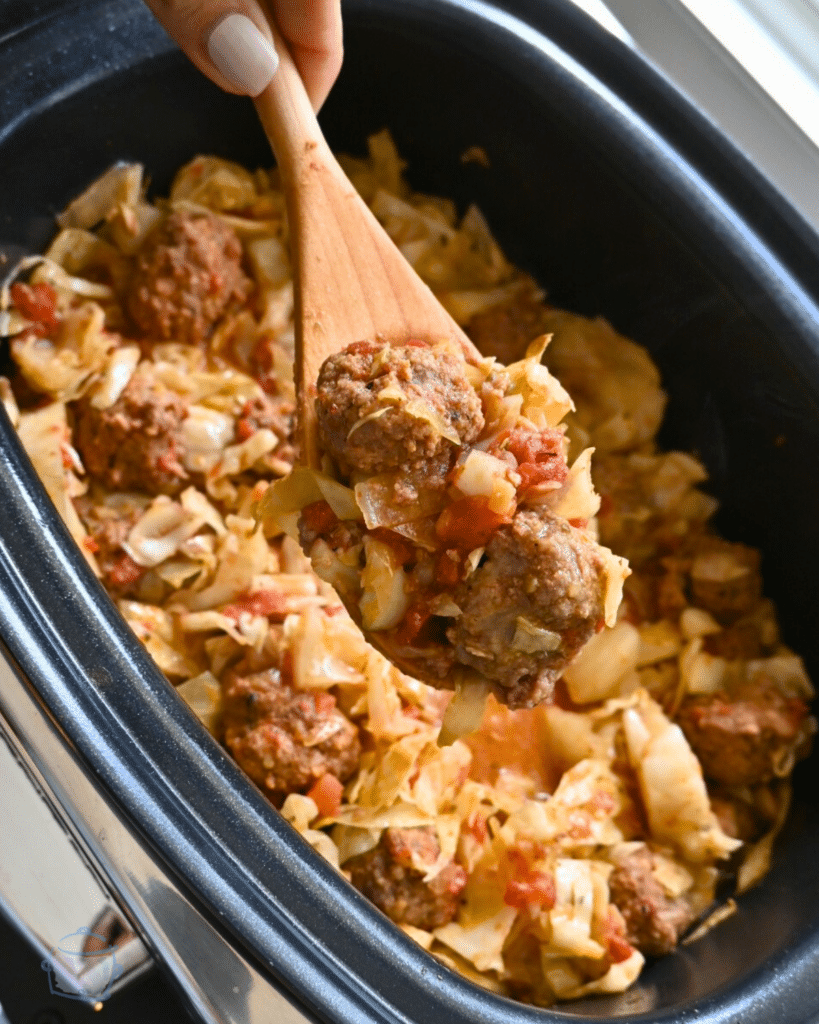 Meatballs and cabbage in a slow cooker with a wooden spoon ready to serve