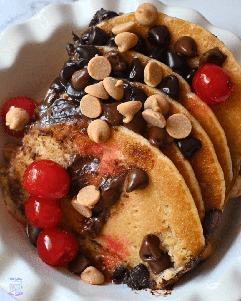 a bowl full of slow cooker chocolate chip pancake casserole topped peanut butter chips and cherries