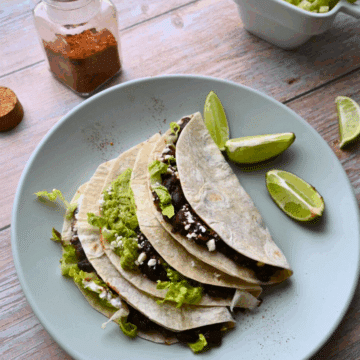 three black bean tacos on a plate with lime wedges