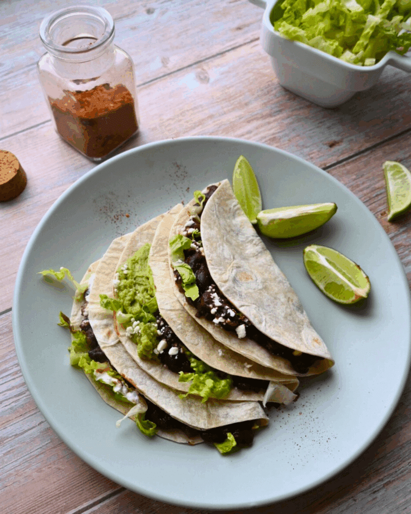 three black bean tacos on a plate with lime wedges