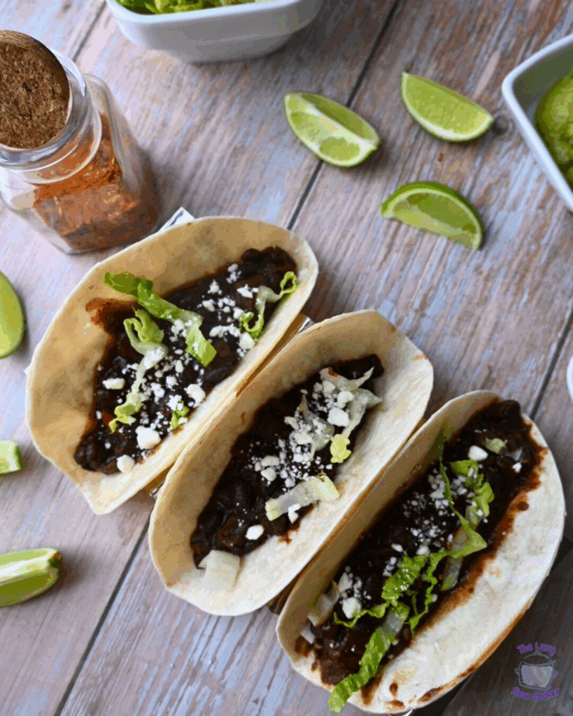 three black bean tacos on a plate with lime wedges