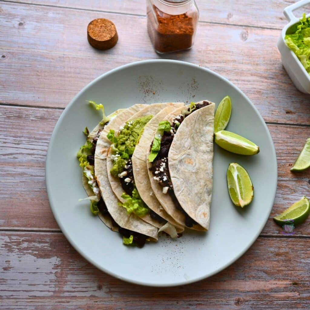 three black bean tacos on a plate with lime wedges