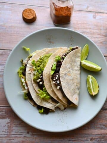 three black bean tacos on a plate with lime wedges