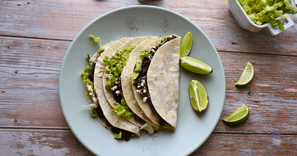 three black bean tacos on a plate with lime wedges