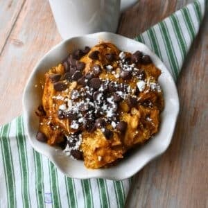 A bowl full of slow cooker pumpkin waffle casserole topped with powdered sugar and chocolate chip