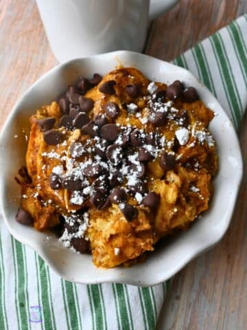 A bowl full of slow cooker pumpkin waffle casserole topped with powdered sugar and chocolate chip
