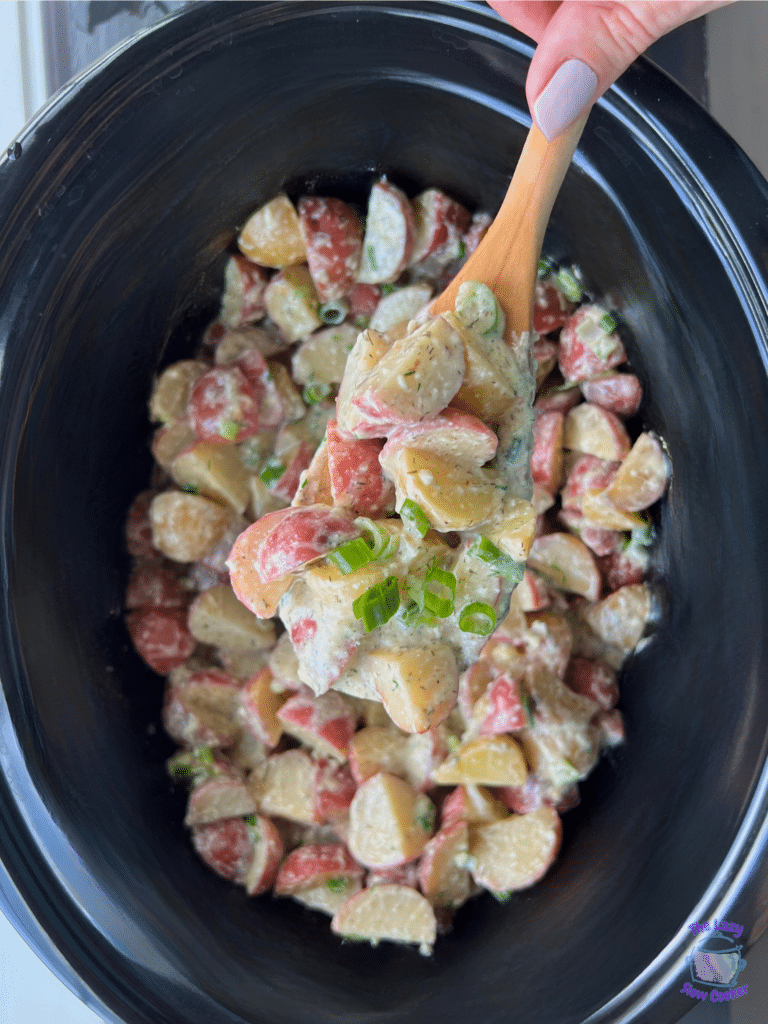 Just cooked warm potato salad on a wooden spoon held over a slow cooker full of the same.