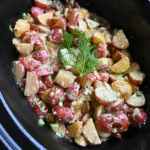 warm potato salad in crock pot after cooking topped with a fresh dill sprig