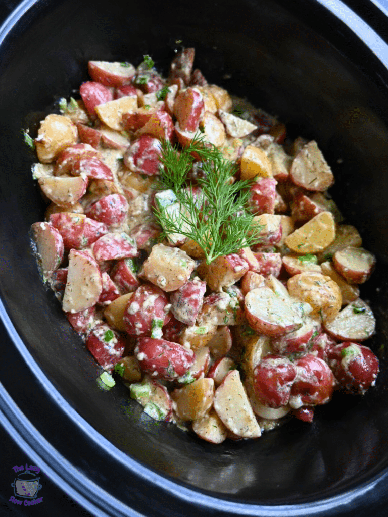 warm potato salad in crock pot after cooking topped with a fresh dill sprig