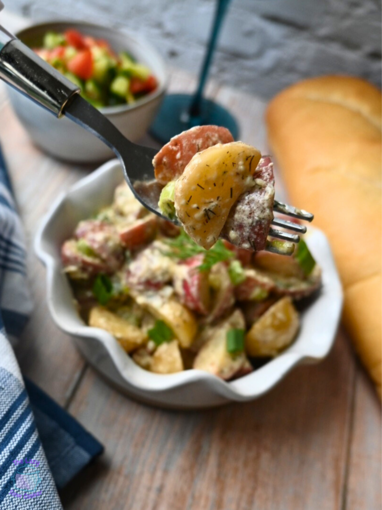 a bowl full of slow cooker warm potato salad. Some is on a fork in the forefront