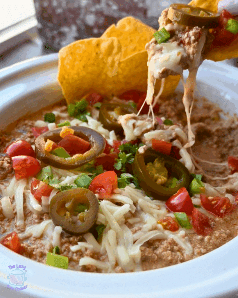 A crockpot full of cottage cheese taco dip with toppings with chips on the side