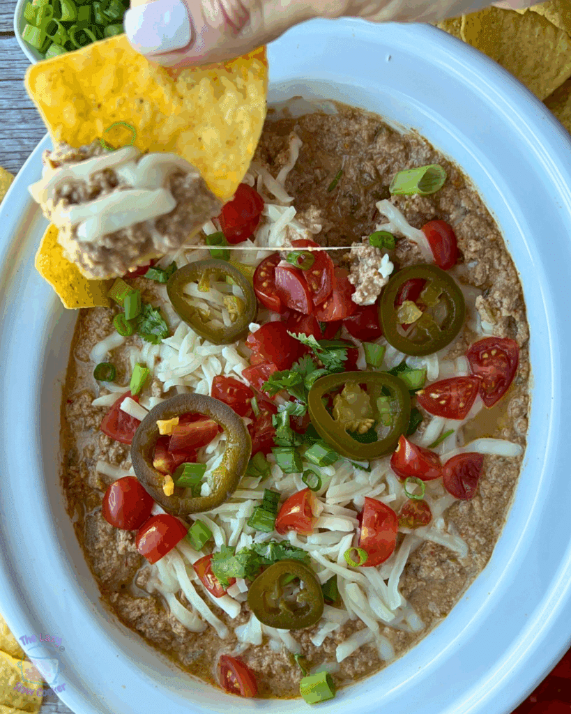 A crockpot full of cottage cheese taco dip with toppings with chips on the side