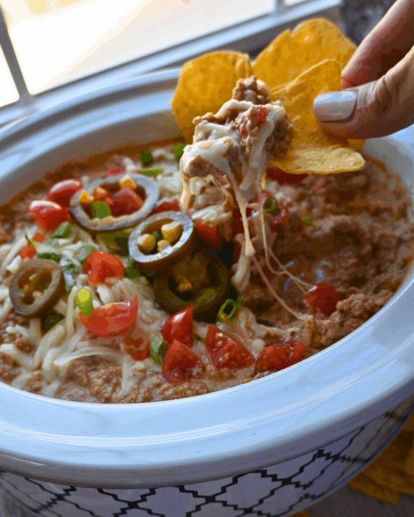 A crockpot full of cottage cheese taco dip with toppings with chips on the side
