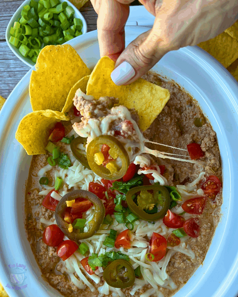 A crockpot full of cottage cheese taco dip with toppings with chips on the side