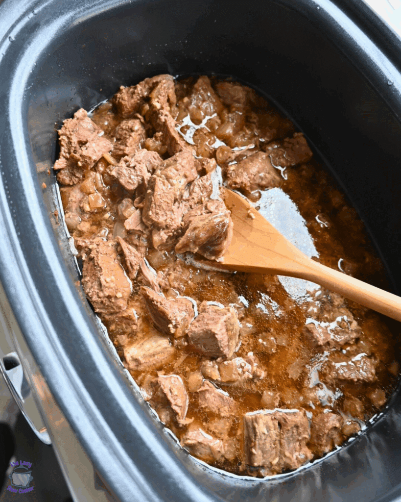cooked steak bites in a crockpot with a slurry of potato starch about to be stirred in.