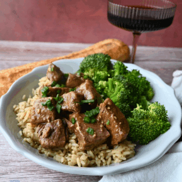 slow cooker steak bites with broccoli on a bed a rice next to a long roll
