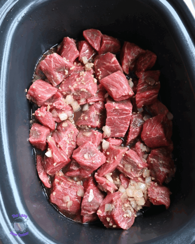 uncooked beef bites in a crock pot with all spices and seasonings