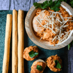 a bowl of slow cooker chicken parmesan dip with a few crackers and breadsticks